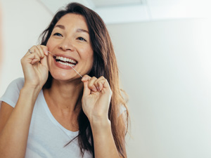 Woman smiling while flossing in bathroom