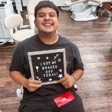 Young man in orthodontic chair holding sign saying I got my braces off today