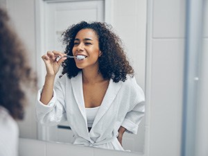 Woman smiling while brushing her teeth in bathroom