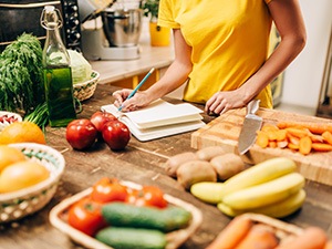 Woman taking notes on counter filled with healthy foods