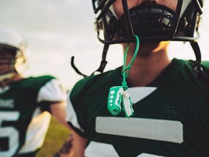 Green mouthguard hanging from football player's helmet