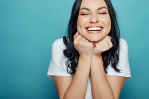 A woman smiling brightly while resting her head on her hands